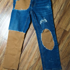 May include: Blue denim jeans with brown fabric patches on the knees and front pocket. The jeans have distressed details and frayed edges.