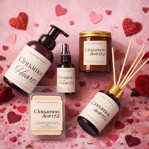 Peut inclure: Divers produits parfumés aux "Cinnamon Hearts", dont une bouteille à pompe, un vaporisateur, une bougie, des fondants parfumés et un diffuseur, disposés sur une surface rose avec des décorations en forme de cœur et des roses. Les produits portent l'inscription "Cinnamon Hearts".
