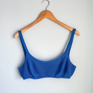 May include: A blue knitted bikini top hanging on a wooden hanger.