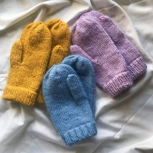 May include: Three pairs of knitted mittens in different colours: yellow, purple, and blue. The mittens are laid out on a white surface.