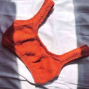 May include: A bright orange knitted crop top with a scoop neck and thin straps.