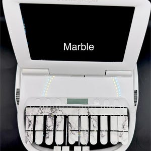 May include: White stenograph machine with a black screen that says "Marble". The machine has a white keyboard with black keys and a white marble design.