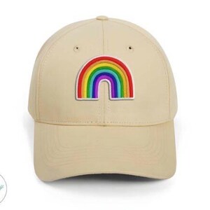 Op de afbeelding: Beige baseballpet met een kleurrijke regenboogpatch. De regenboog heeft de kleuren rood, oranje, geel, groen, blauw en paars. De pet heeft een gebogen klep en een knoop aan de bovenkant.