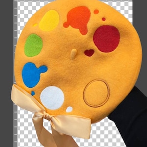 Könnte beinhalten: Senfgelber Barett mit bunten Farbspritzern in Rot, Orange, Gelb, Grün, Blau und Weiß. Eine passende Schleife ist am unteren Rand des Baretts gebunden. Der Text "palette.beret" ist oben links sichtbar.