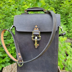 May include: A black leather satchel bag with a brown leather strap and a silver buckle. The bag has a top handle and a shoulder strap.