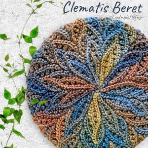 Puede incluir: Un gorro de punto de crochet en tonos azules, amarillos y marrones con un patrón floral texturizado. El gorro se llama "Clematis Beret" y es de @liudmylahefny.