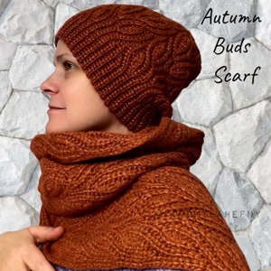 Puede incluir: Un conjunto de gorro y bufanda de punto de color &oacute;xido. El gorro es de estilo beanie y la bufanda es una capucha. El conjunto est&aacute; hecho con un patr&oacute;n de punto de cable. El texto "Autumn Buds Scarf" es visible en la imagen.