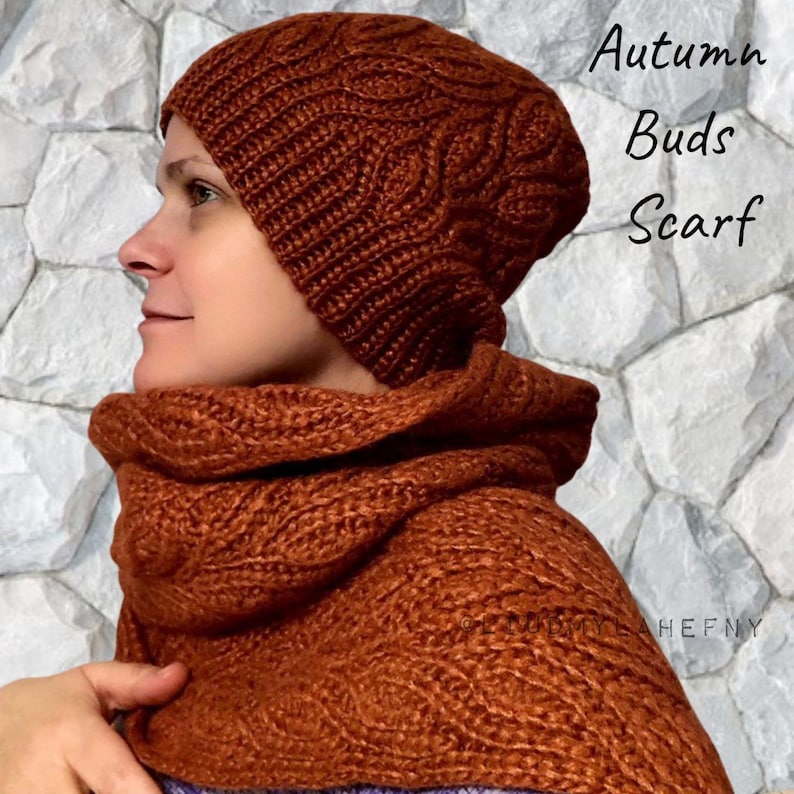 Puede incluir: Un conjunto de gorro y bufanda de punto de color &oacute;xido. El gorro es de estilo beanie y la bufanda es una capucha. El conjunto est&aacute; hecho con un patr&oacute;n de punto de cable. El texto "Autumn Buds Scarf" es visible en la imagen.