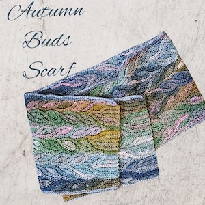 Puede incluir: Una bufanda de ganchillo con un patr&oacute;n de hojas en tonos de azul, verde, amarillo y rosa. La bufanda est&aacute; doblada por la mitad y el texto "Autumn Buds Scarf" est&aacute; escrito encima.