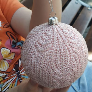 May include: A pink knitted Christmas bauble with a silver hanger. The bauble has a cable knit pattern and a sparkly finish.