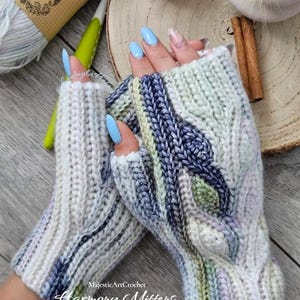 May include: A pair of fingerless mittens featuring a complex cable knit pattern in variegated shades of cream, sage green, and slate blue. The mittens have a ribbed cuff and a thumb opening, showcasing a textured, multi-colored yarn construction.