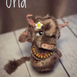 May include: A brown and black plush toy cow with a white flower on its head. The cow has a beaded necklace and a long tail. The word "Grid" is written in white on a brown background.
