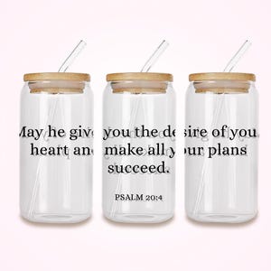 Puede incluir: Tres vasos de vidrio transparente con tapas de madera y pajitas transparentes. Cada vaso tiene el texto "May he give you the desire of your heart and make all your plans succeed. Psalm 20:4" impreso en negro.