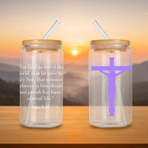 Puede incluir: Dos vasos de vidrio transparente con forma de lata con tapas y pajitas de bambú. Uno tiene un gráfico de cruz morada, el otro tiene un versículo bíblico blanco. El fondo es una puesta de sol sobre montañas.