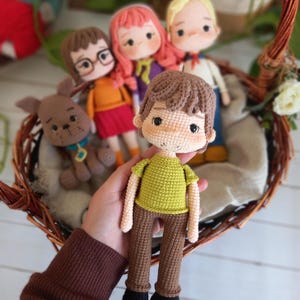 Puede incluir: Un grupo de muñecas de crochet, que incluye un perro marrón, una niña con el pelo rojo, una niña con el pelo marrón que lleva gafas, un niño con el pelo rubio y un niño con el pelo marrón que lleva una camisa verde y pantalones marrones.