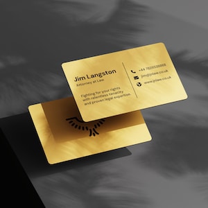 May include: Two gold business cards with rounded corners. The top card displays contact information for Jim Langston, Attorney at Law, including a phone number, email, and website. The bottom card shows a logo. The cards are on a dark grey surface.