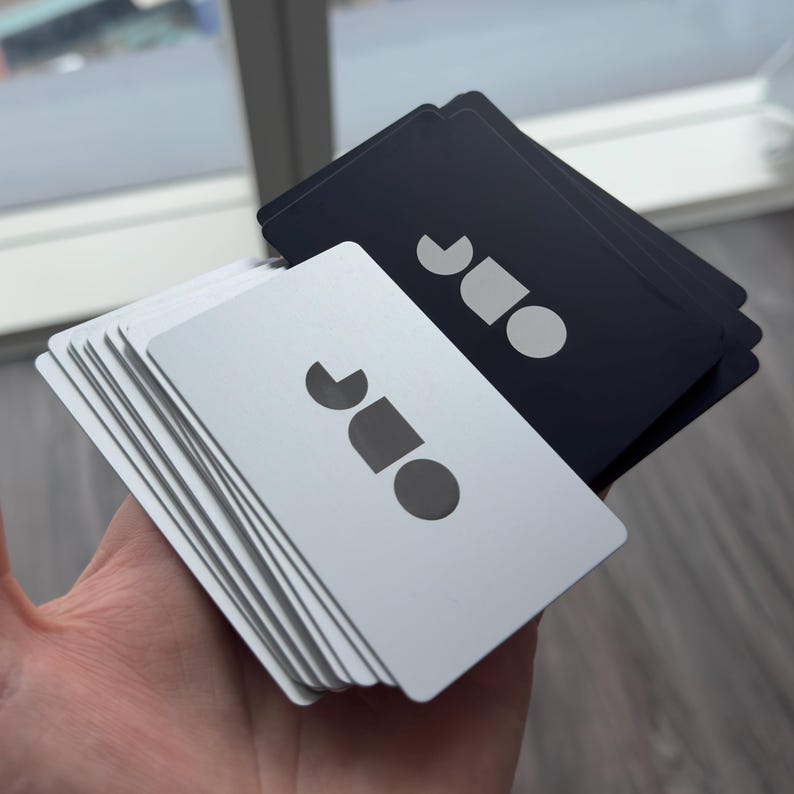 May include: A hand holding a stack of white business cards and a stack of black business cards. Each card features a logo with a semi-circle, a square, and a circle.