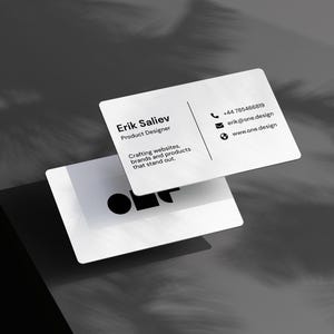 May include: Two white business cards with rounded corners. The top card displays the name "Erik Saliev, Product Designer" and contact information. The bottom card shows a graphic logo. The cards are on a grey surface with shadow details.