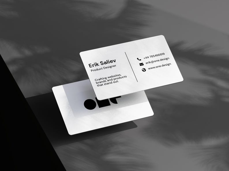 May include: Two white business cards with rounded corners. The top card displays the name "Erik Saliev, Product Designer" and contact information. The bottom card shows a graphic logo. The cards are on a grey surface with shadow details.