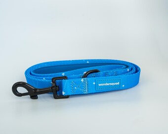May include: A rolled-up blue dog leash with a black clasp and a white star pattern. The leash has the text "wondersquad" on a white rectangular patch. The leash is made of a durable material.
