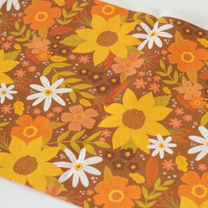May include: A roll of floral patterned paper featuring a repeating design of sunflowers, daisies, and other flowers in shades of yellow, orange, and white on a brown background. The paper is partially unrolled.