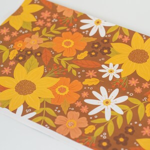 May include: A sheet of paper with a repeating floral pattern. The design features large yellow sunflowers, orange and white flowers, and green leaves on a brown background. The overall theme is autumnal.