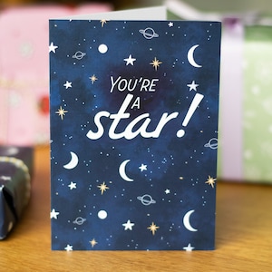 May include: A blue card with a white starry night sky design and the text "You're a star!" in white.