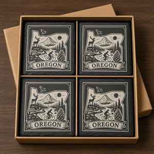 May include: Set of four black slate coasters with a white graphic of the Oregon state outline, mountains, a cyclist, and the word "OREGON". The coasters are in a brown cardboard box.