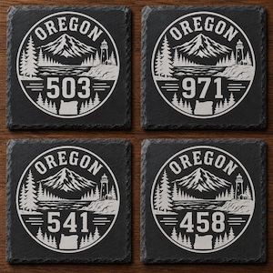 May include: Four square black slate coasters with a white graphic design. Each coaster features the word "OREGON" in a circle, with a mountain, trees, lighthouse, and a state outline. Each coaster has a different area code: 503, 971, 541, and 458.