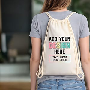 May include: A cream-colored drawstring backpack featuring the black text ADD YOUR DESIGN HERE, with the word DESIGN in a pastel gradient, and a rectangular box below containing the text TEXT - PHOTO IMAGE - LOGO in black lettering.