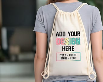 以下が含まれることがあります： クリーム色の巾着型バックパック。黒い文字で「ADD YOUR DESIGN HERE」と書かれており、「DESIGN」の文字はパステルカラーのグラデーションになっています。その下には「TEXT - PHOTO IMAGE - LOGO」と記された黒い枠があります。