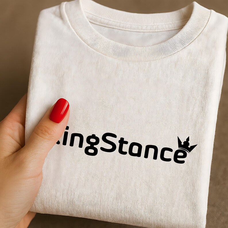 Puede incluir: Camiseta crema doblada con el texto negro "ingStance" y un dise&ntilde;o de corona. La tela parece suave y c&oacute;moda. El dise&ntilde;o se muestra claramente en la parte delantera.