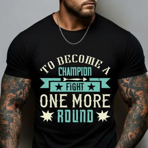 May include: Black t-shirt with the text "TO BECOME A CHAMPION FIGHT ONE MORE ROUND" in white and teal. The design includes stars and an arrow. The shirt is a crew neck style.