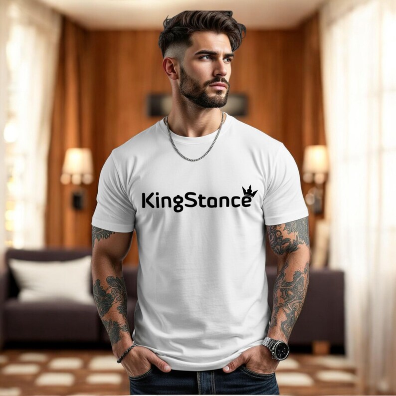 Puede incluir: Camiseta blanca de cuello redondo con el texto "KingStance" en negro y un gr&aacute;fico de corona. La persona que lleva la camiseta tiene tatuajes en los brazos y un collar de cadena plateada.