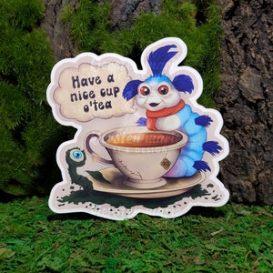 May include: A blue and white cartoon caterpillar wearing a red scarf is holding a teacup with a teabag. The caterpillar is sitting on a saucer with a green leaf and a small green eye. The text "Have a nice cup o'tea" is in a speech bubble above the caterpillar.