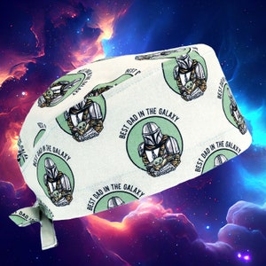 May include: A white scrub hat with a repeating pattern of a green and gray Mandalorian character holding a small green alien. The text "Best Dad in the Galaxy" is printed in a circle around each character.