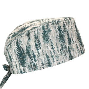 Puede incluir: Un gorro quirúrgico con estampado de bosque en tonos verdes y grises. El gorro tiene un cierre de lazo en la parte posterior y está hecho de una tela suave estampada. El diseño incluye un patrón repetido de árboles de hoja perenne estilizados.