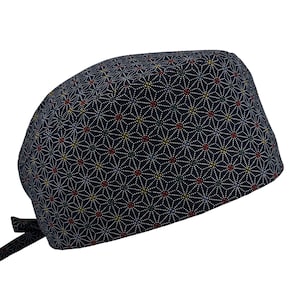 Puede incluir: Un gorro quirúrgico azul marino con un patrón geométrico repetitivo en blanco, rojo y amarillo. El gorro tiene un cierre de lazo en la parte posterior. El patrón es una serie de formas de estrella.