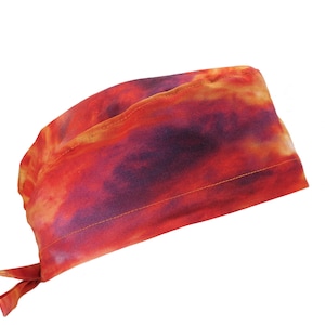 May include: A tie-back scrub cap with a vibrant tie-dye pattern in shades of red, orange, and purple. The cap is made of soft fabric and features a tie closure for a secure fit. Suitable for medical professionals or anyone needing a stylish head covering.