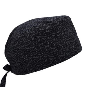 Puede incluir: Un gorro quirúrgico azul marino oscuro con un patrón repetido de pequeños semicírculos grises claros. El gorro se ata en la parte posterior con dos largas cintas de tela.