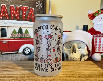 May include: White frosted tumbler with a black and white illustration of skeletons wearing Santa hats and holding Christmas gifts. The text on the tumbler reads "When you're dead inside but it's the holiday season".