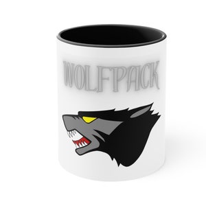 May include: White ceramic mug with a black rim. The mug has a gray wolf head with yellow eyes and red teeth. The text "WOLFPACK" is printed in gray on the mug.