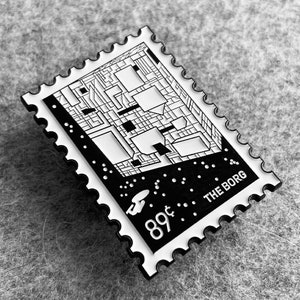 May include: Black and white enamel pin featuring a stylized image of the Borg Cube from Star Trek. The pin has a white border with the text "89¢ THE BORG" printed on it.