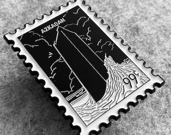 May include: Black and white enamel pin featuring a stylized illustration of a tall building with the text "Azkaban" and "99¢" on a white postage stamp.