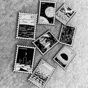 May include: A set of ten black and white enamel pins featuring different cityscapes and space-themed designs. Each pin has a different price printed on it, such as 97&cent;, 77&cent;, 72&cent;, 99&cent;, 92&cent;, 82&cent;, and 9&cent;. The pins are arranged on a gray textured surface.
