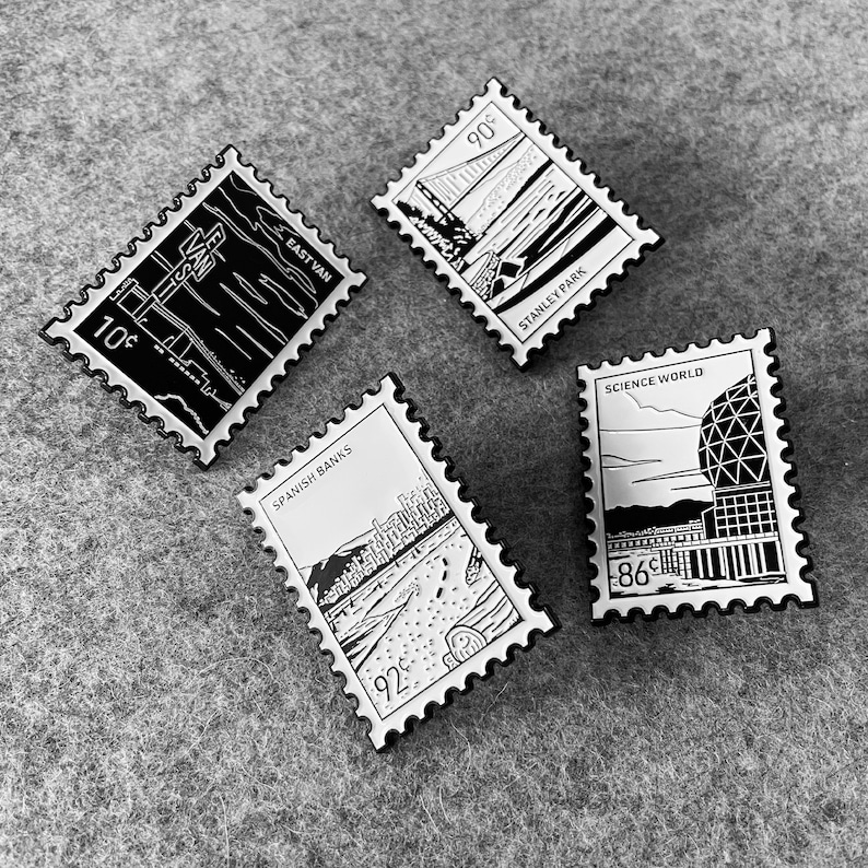 May include: Set of five enamel pins featuring black and white illustrations of landmarks in Vancouver, Canada. The pins are shaped like postage stamps and feature the following text: "East Van", "Stanley Park", "Science World", "Spanish Banks", and "90&cent;".