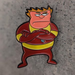 May include: An enamel pin featuring a cartoon character with a grumpy expression. The character has red skin, yellow hair, and is wearing a red and yellow suit.