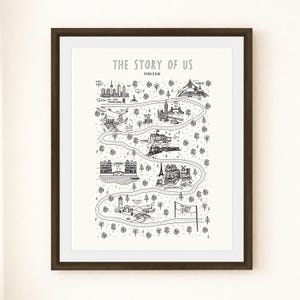 May include: Framed black and white art print titled "The Story of Us." The artwork shows a winding road with illustrated landmarks and location names. The print is in a dark brown frame with a white mount.