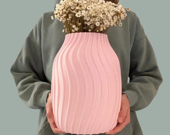 May include: A light pink vase with a vertical wavy, ribbed texture. The vase is filled with a large bouquet of small, dried white flowers with yellow centers. The object has a rounded, bulbous shape that tapers slightly toward the top opening.