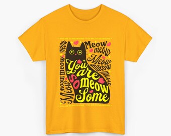 Puede incluir: Camiseta de color amarillo mostaza con una ilustración de un gato negro y la frase "You are meow some". El diseño incluye corazones rosas y la palabra "meow" repetida. Una divertida camiseta gráfica con temática de gatos.